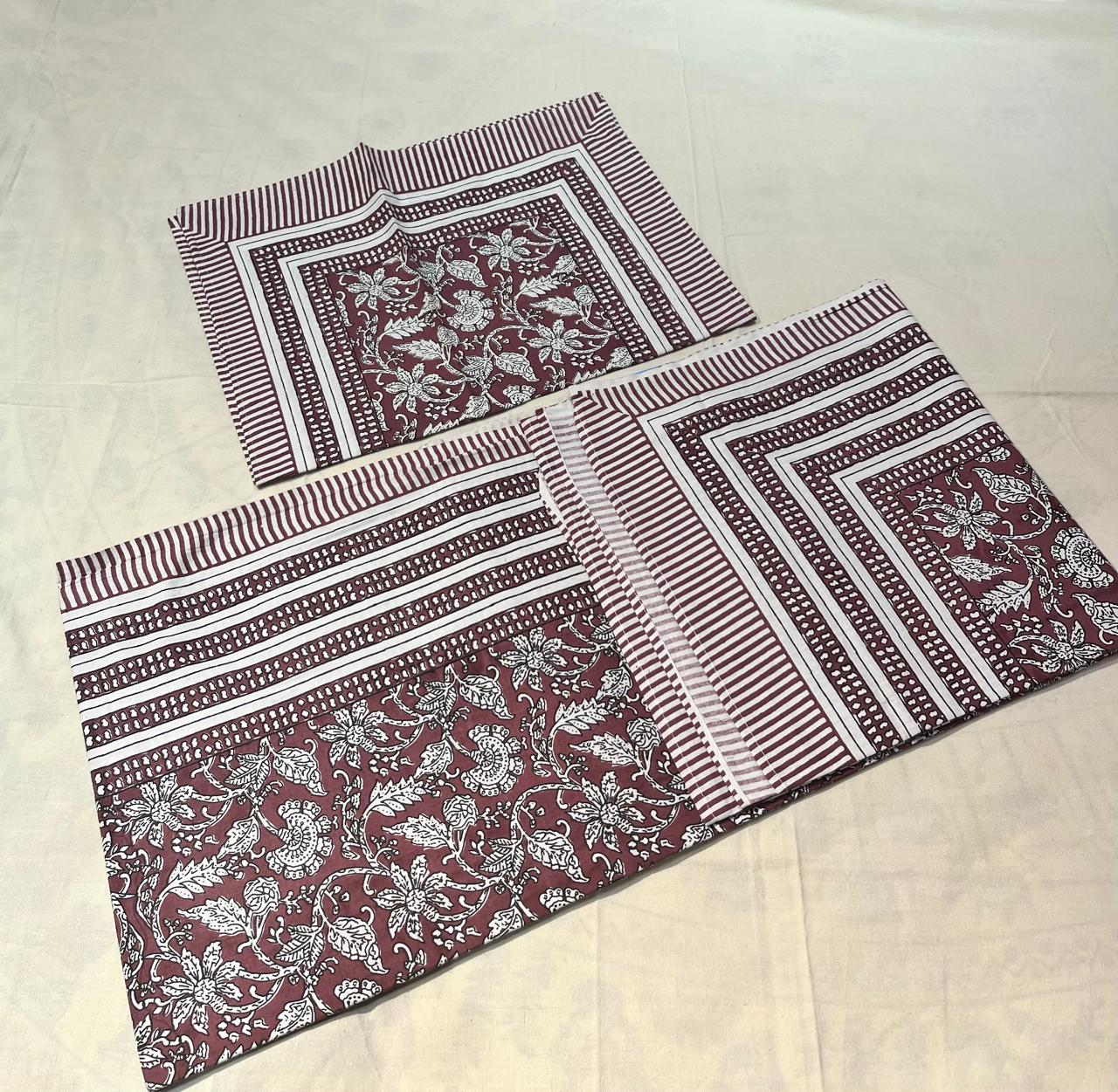 Two fabric placemats with floral and striped patterns on a beige surface